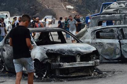 Varias personas inspeccionan los vehículos quemados tras los voraces incendios forestales en Bouira, Argelia, el pasado lunes.