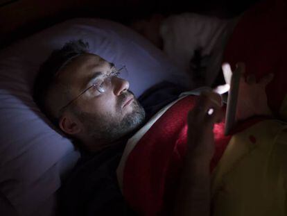 Un hombre lee a oscuras con su smartphone en la cama.