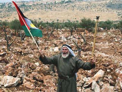 Un habitante de Cisjordania ondea un bandera palestina en un campo a punto de ser atravesado por el muro.