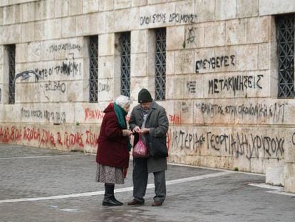 Una pareja de ancianos comprueban las monedas que les quedan junto a la fachada con pintadas de la Universidad de Atenas.