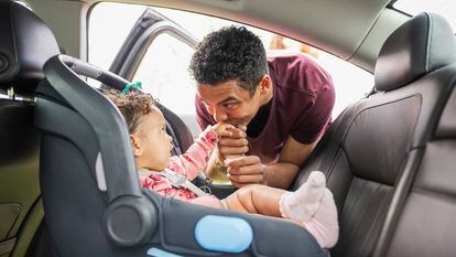 Padre joven poniendo a la niña en el asiento del coche.