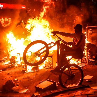 A demonstrator rides a bike at a barricade set on fire during clashes with riot police which erupted during a protest against the death of a lawyer under police custody, in Bogota, early on September 10, 2020. - A man who was detained by police officers died Wednesday in Bogota after receiving repeated electric shocks on the ground with a stun gun. (Photo by STR / AFP)