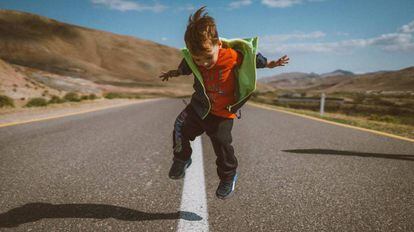 Un niño salta en medio de una carretera vacía. 