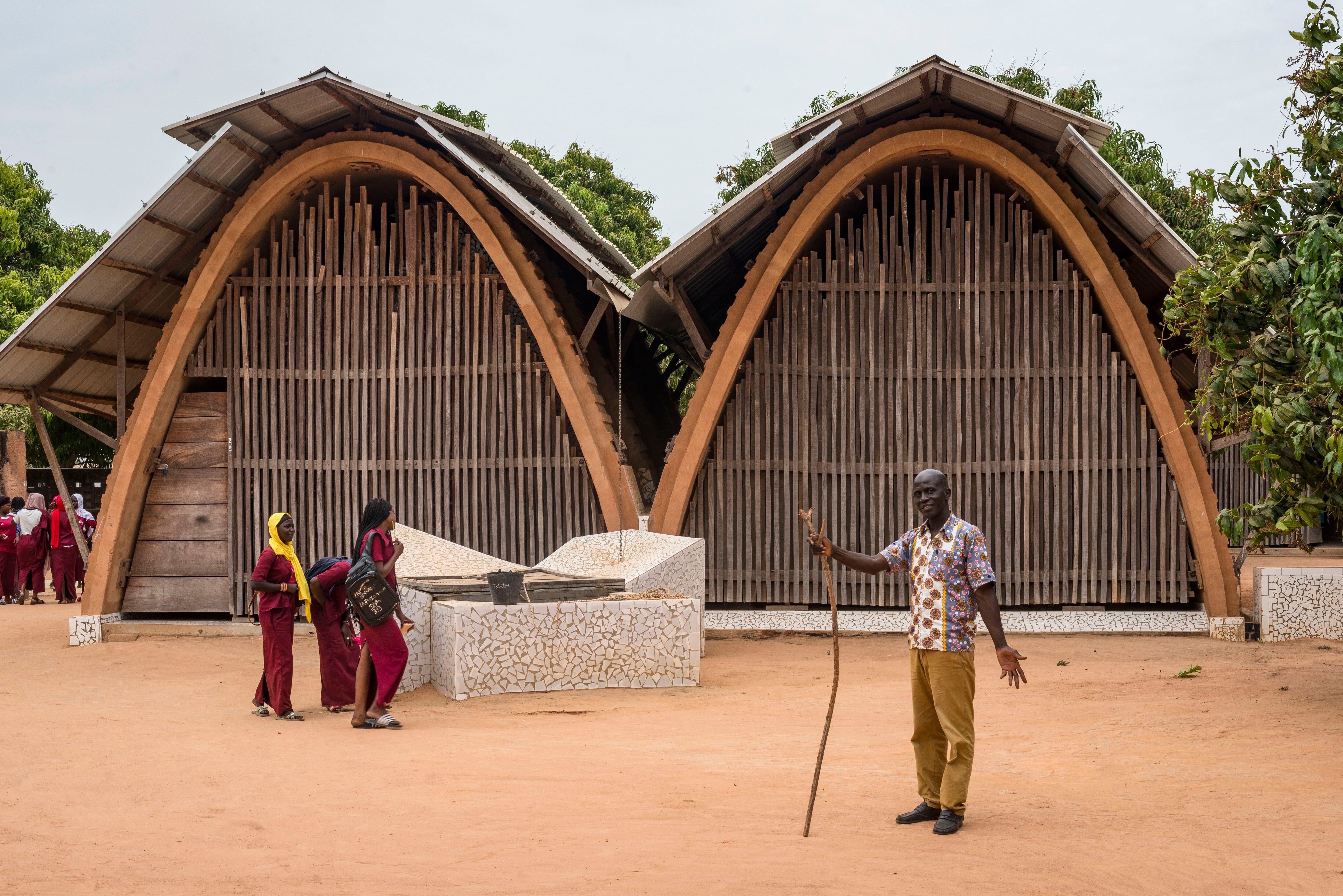El jefe de estudios de la escuela Kamanar, Cheikh Malick Camara, en la localidad senegalesa de Thionck Essyl, posa frente a dos de las 16 aulas que forman parte del complejo educativo. Las construcciones se distribuyen en grupos de cuatro por un amplio espacio de dos hectáreas salpicado de árboles.