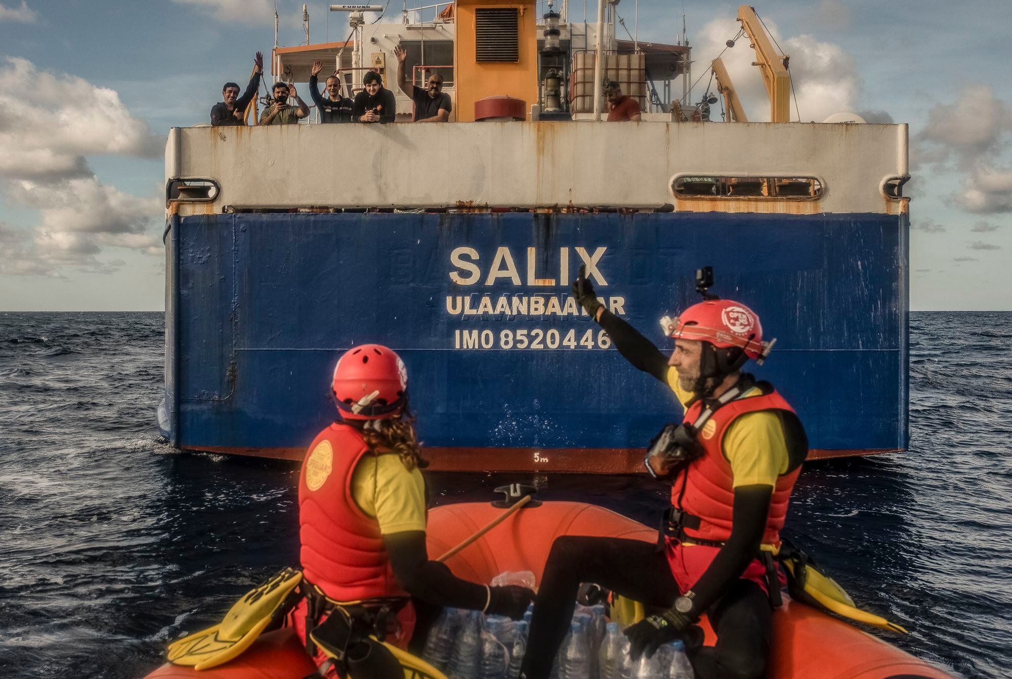 Un barco mercante, de bandera de Mongolia y nombre SALIX, que se encontraba en la zona de rescate, acompañó al equipo de socorristas de Open Arms mientras brindaba ayuda según el protocolo de los tratados internacionales de la Organización Internacional para las Migraciones, proporcionando agua, galletas y mantas para los voluntarios de la ONG española y los tripulantes del bote en peligro.