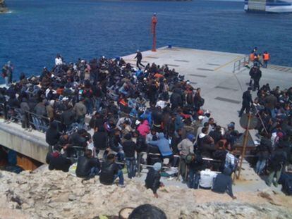 Un grupo de inmigrantes observa las maniobras de un barco que intenta atracar, con dificultades por el mal estado del mar, en la isla de Lampedusa.