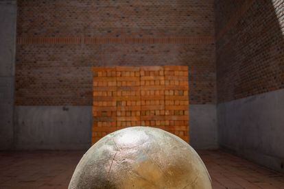 Un cubo de ladrillos y una esfera de arcilla cubierta en oro en un patio del estudio.