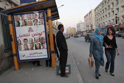 Unas mujeres pasan junto a una parada de autobuses con un cartel electoral que reza Túnez vota.