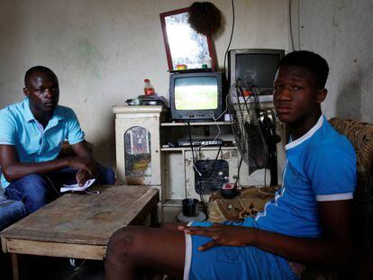 Abdoulaye Dosso (izq.) regresó de Libia voluntariamente. Se sienta junto a un pariente en su casa en Abiyán.