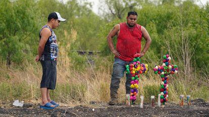 Dos hombres bajo la lluvia contemplan el memorial improvisado cerca del sitio donde fue encontrado el camión de remolque con los migrantes hacinados, el 28 de junio, en San Antonio, Texas, (EEUU).