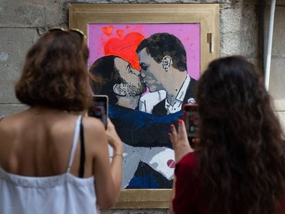 Dos mujeres fotografían la obra del artista urbano Salvatore Benintende, donde Pedro Sánchez y Pablo Iglesias se dan un beso, en Barcelona.