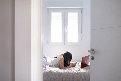 Una joven mira su ordenador y móvil en su habitación.