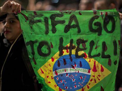Un manifestantes con una bandera de Brasil en la que se lee "FIFA, vete al infierno".