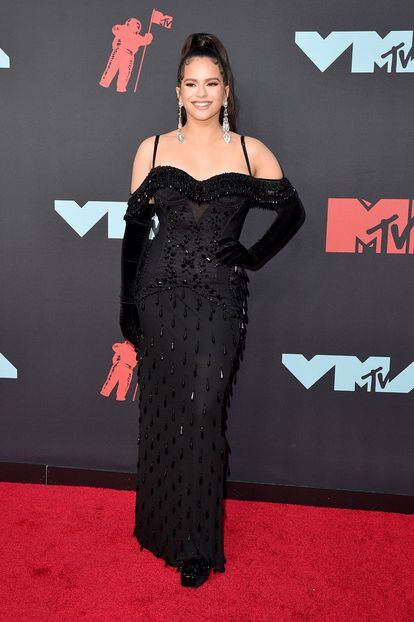 Rosalía posó en la alfombra roja de los MTV VMA's con un vestido hecho a medida por Burberry. El modelo, negro satinado y con volantes, incluía lágrimas de cristal. El look se completó con unos guantes de terciopelo.