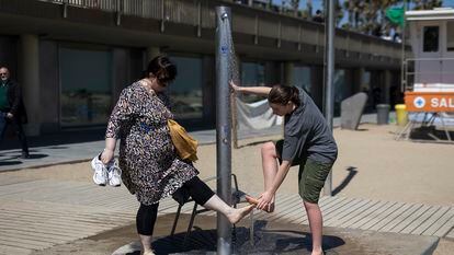 Dos personas se lavan los pies en una ducha de la playa de la Barceloneta.