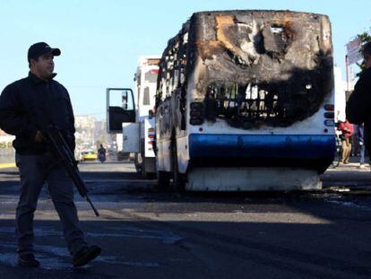 Un policía junto a uno de los autobuses incendiados durante un operativo en contra del CJNG en la ciudad de Zapopan en 2014.