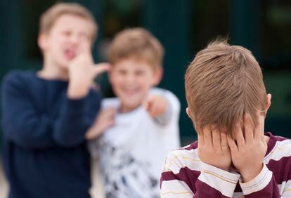 Dos niños se ríen de otro en el patio del colegio.