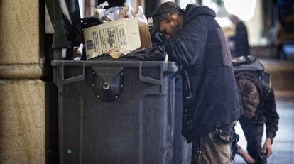 Dos personas buscan restos en un cubo de basura