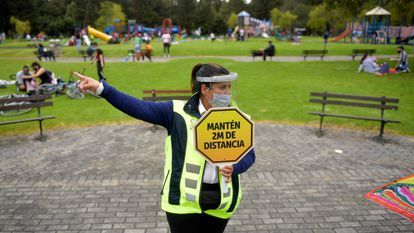 Una vigilante de seguridad con un cartel pidiendo distancia de seguridad, en un parque de Bogotá (Colombia).