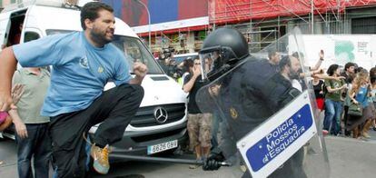 Uno de los manifestantes intenta evitar el golpe de un mosso d'esquadra durante el desalojo de los acampados en la plaza Cataluña de Barcelona