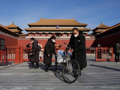 Trabajadores con mascarillas empujan un triciclo con comidas y bebidas frente a la Ciudad Prohibida de Pekín el 14 de diciembre.