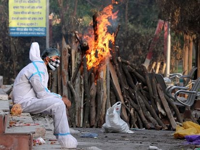 Un hombre ataviado con un traje aislante permanece sentado tras realizar rituales funerarios a sus familiares difuntos, el lunes en Nueva Delhi.