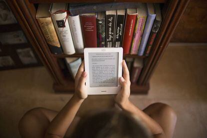 Una chica lee un 'e-book' junto a varios libros.