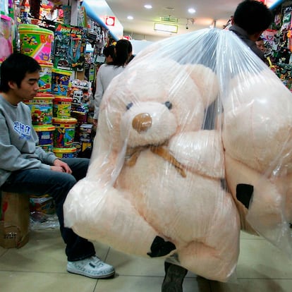 Un trabajador transporta osos de peluche dentro de una bolsa en una tienda durante la época navideña.