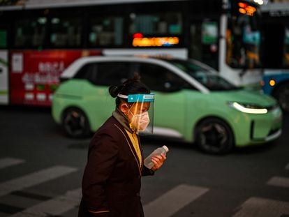 Una mujer con mascarilla y pantalla protectora pasea por el barrio de Huangpu en Shanghái (China).