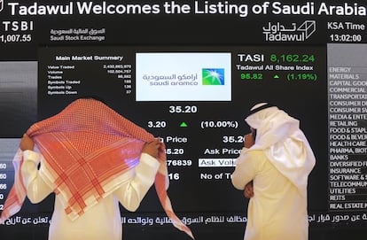 Dos hombres observan un panel de cotización de Saudi Aramco en la Bolsa de Riad.