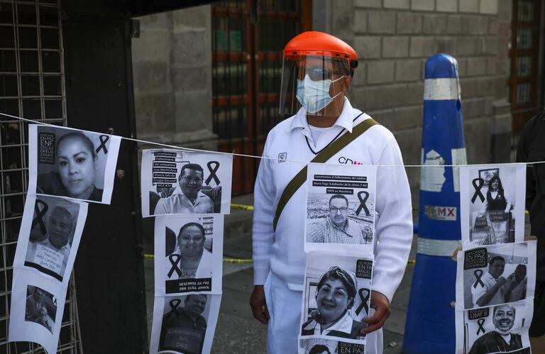 A hospital worker stands with images of colleagues who have died from COVID-19 during a protest in front of the National Palace in Mexico City, Friday, May 29, 2020. Doctors, nurses and other personnel have demonstrated at a number of public hospitals around the country as the new coronavirus sickens medical personnel. (AP Photo/Eduardo Verdugo)