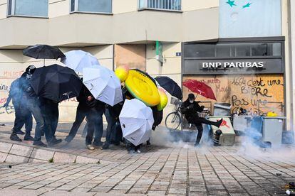 Un manifestante chuta un bote de gas lacrimógeno, mientras otros usan paraguas como escudos durante los enfrentamientos con la policía en Nantes.