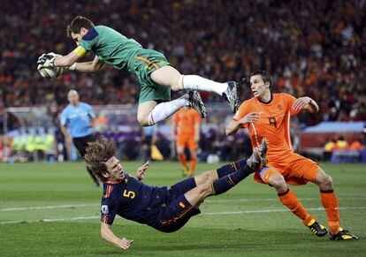 El portero español, Iker Casillas vuela tras atrapar el balón después de un choque con Puyol ( abajo) , ante el jugador holandés Van Persie ,en el partido de la final de la Copa del Mundo de Sudáfrica 2010, donde España gano a Holanda por 1- 0, a cuatro minutos del final de la prórroga, en el estadio Soccer City, en Johanesburgo.