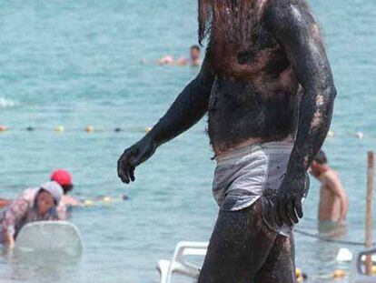 Un judío ultraortodoxo pasea por una playa del mar Muerto totalmente cubierto de barro.