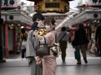 Visitantes protegidos con mascarillas se toman selfis en un centro comercial del distrito de Asakusa, en Tokio (Japón).