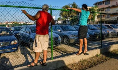 Un par de cubanos observan un lote de autos usados en venta. 