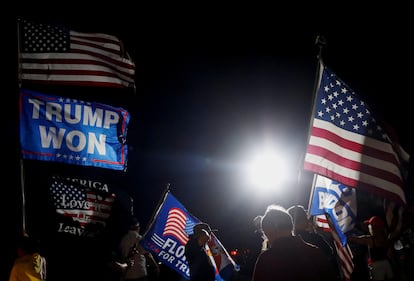 Los partidarios del expresidente de Estados Unidos, Donald Trump, sostienen banderas mientras se reúnen frente a su casa, el lunes.