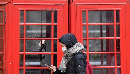 Una mujer con mascarilla protectora revisa su teléfono móvil mientras camina por Londres.