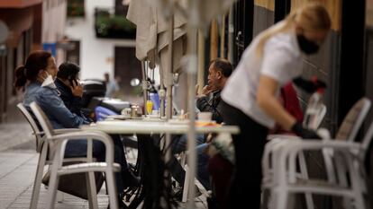 Una camarera de una cafetería de Santa Cruz de Tenerife limpia una mesa mientras varios clientes toman sus consumiciones.