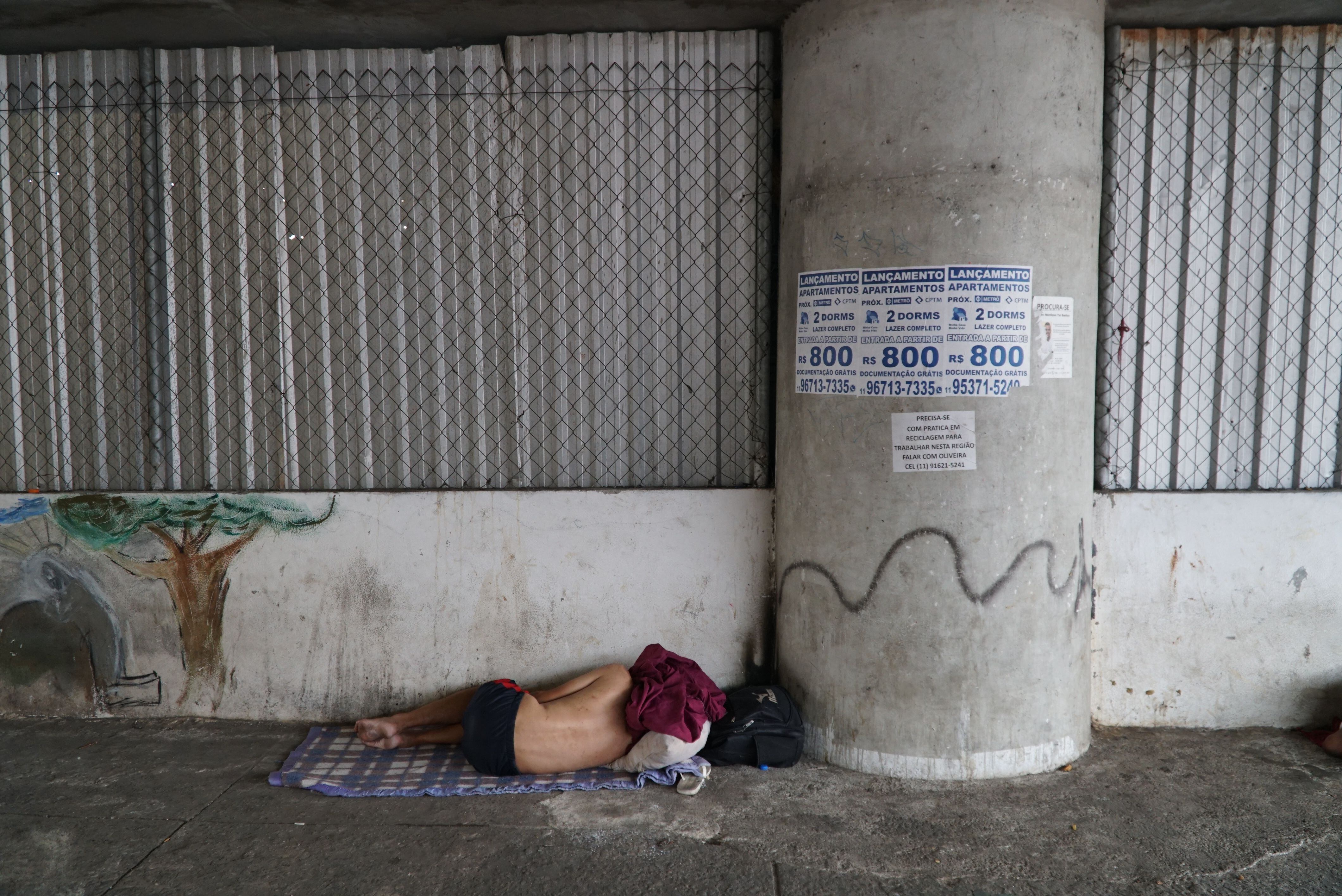 Un hombre duerme en la acera junto a la valla que cierra el espacio bajo un viaducto en São Paulo