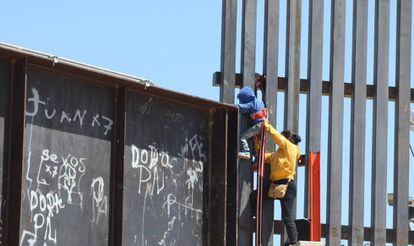 Una mujer ayuda a su hijo a trepar la valla fronteriza que divide a México y Estados Unidos.