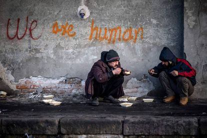 Dos migrantes se alimentan con comida recibida por voluntarios, en un almacén a las afueras de Belgrado (Serbia).