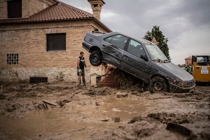 Unos vecinos limpian su casa después de que la riada rompiese un muro y dejase un coche encallado.