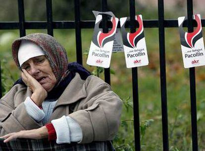 Una mujer, sentada en una calle de Pristina, con carteles electorales colgados detrás.