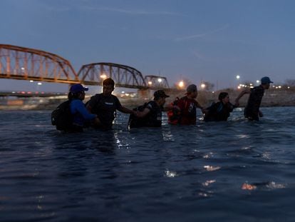 Migrantes se enlazan de brazos mientras vadean el Río Grande con intenciones de cruzar a Eagle Pass (Texas).