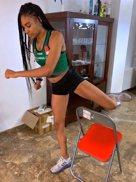 La futbolista y atleta Salma Paralluelo, entrenando con una silla en su casa la técnica del salto de valla.