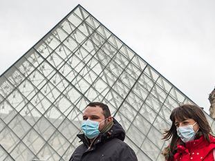 Dos personas con mascarillas pasan frente al Museo del Louvre de París.