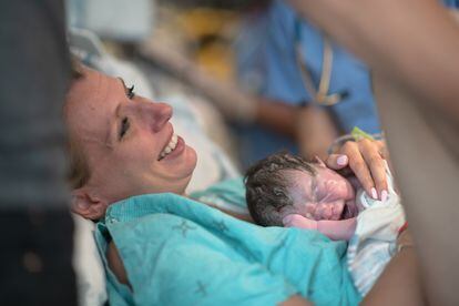 Una madre sonríe mientras sostiene a su bebé recién nacido por primera vez en su pecho.