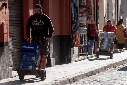 Dos operarios con carretillas con botellines de Mahou y alcohol y barriles de cerveza este viernes en Sevilla.