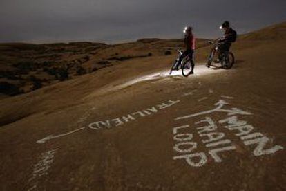 Dos ciclistas recorren el Slickrock trail, en Moab (Utah), en una noche de luna llena.